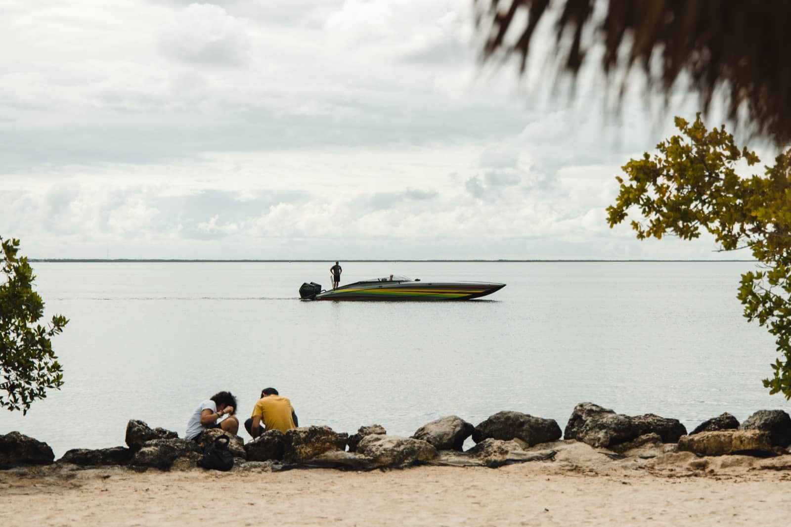 Friends sitting on rocks at the water's edge watching a boat cross the bay